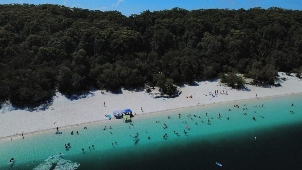 Aerial shot of the blue waters of Lake Mackenzie with lots of people dotted on the beach and in the water.