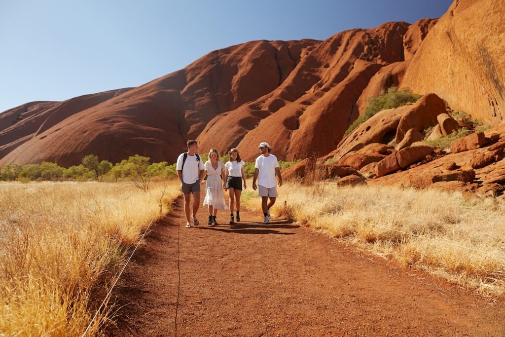 Image shows four people walking through the Red Centre on a group tour.