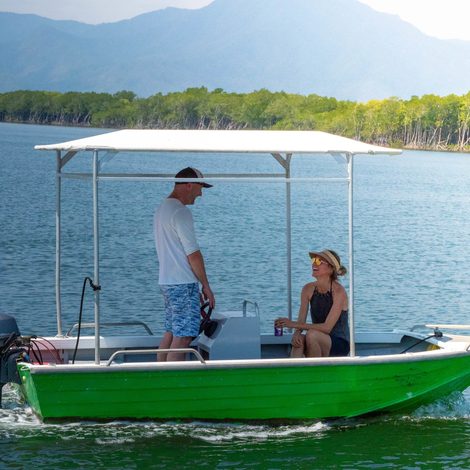 Tinny boat on Trinity Inlet with two people on board and views of the mountains behind them.