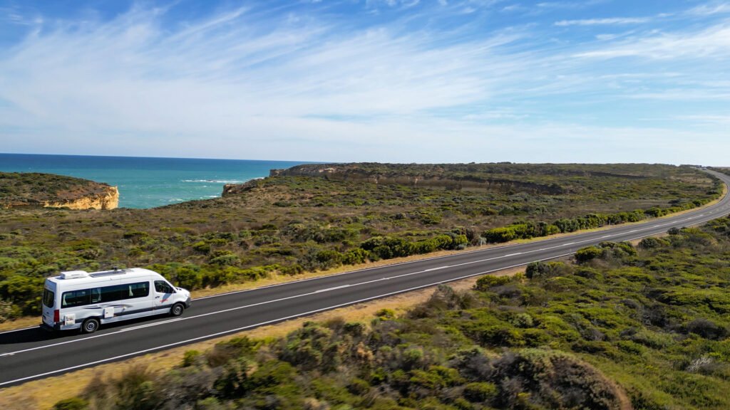 Wide shot of a campervan driving along a road on the Great Ocean Road road trip.