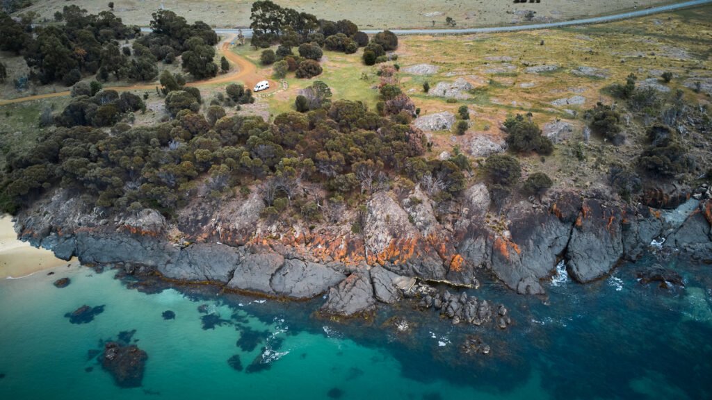 Birdseye view of a campervan parked on a cliff edge by the sea.