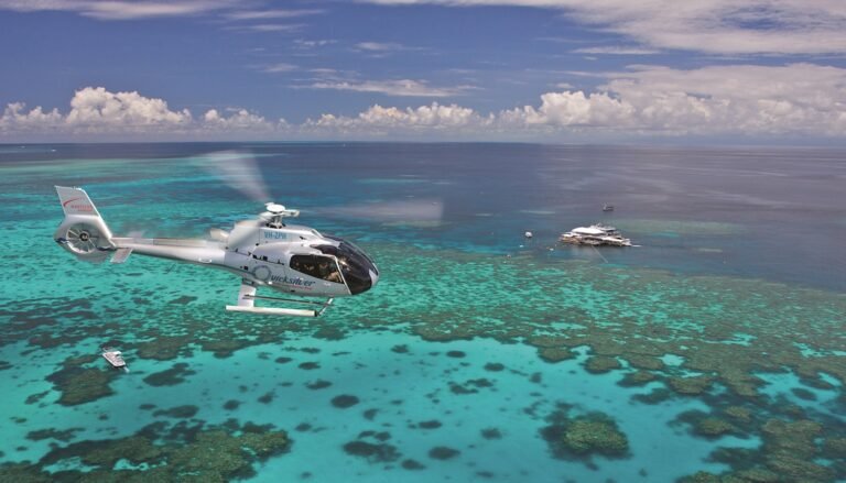 A wide shot of a helicopter flying over the Great Barrier Reef with the boat in the distance.