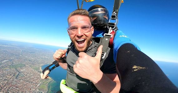 Image shows a backpacker skydiving looking excited.