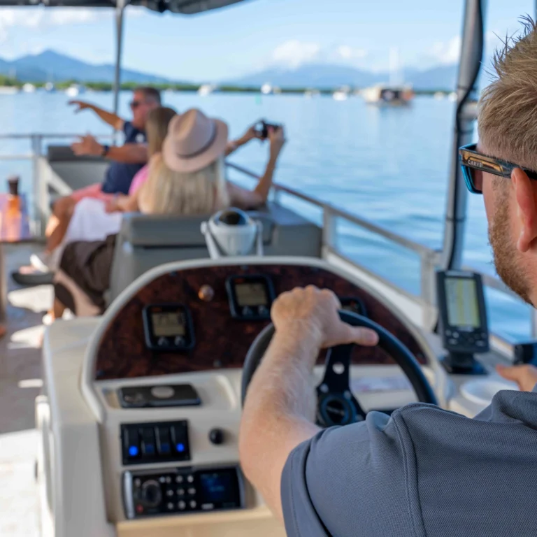 A man is driving a boat along Trinity Inlet whilst passengers in front are taking pictures.