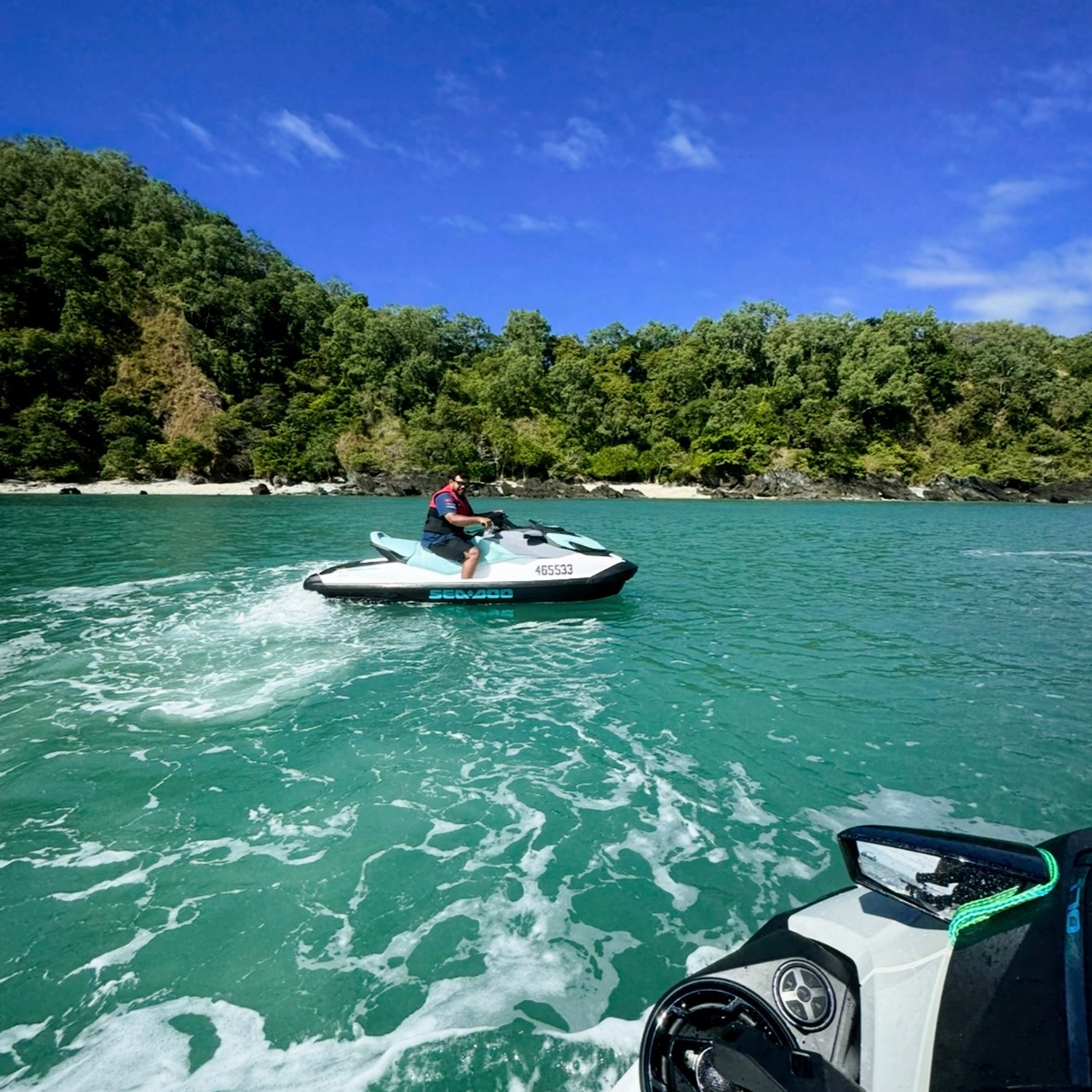 Wide shot of a person riding a jet ski along the coastline on a jet ski tour.