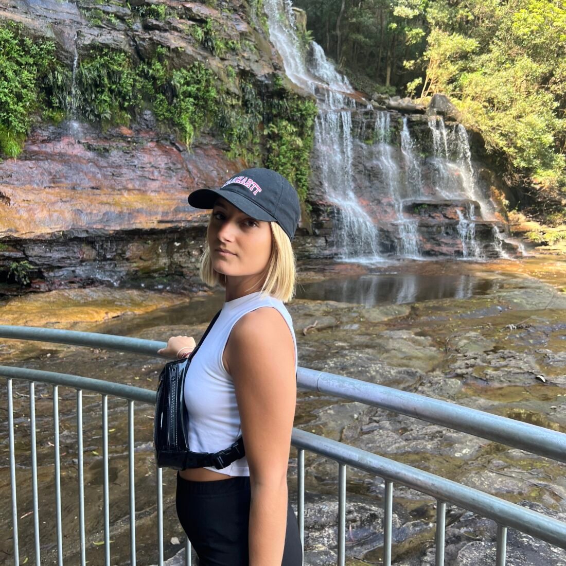 Image shows a woman posing in front of a waterfall.