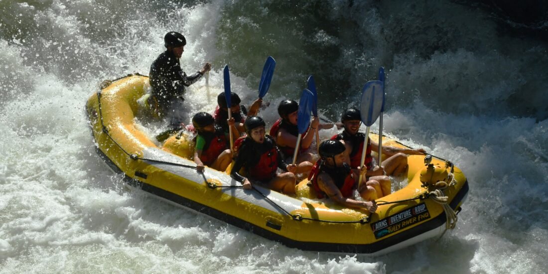 Group of rafters wearing helmets and life jackets navigating whitewater rapids on the Tully River in Far North Queensland.