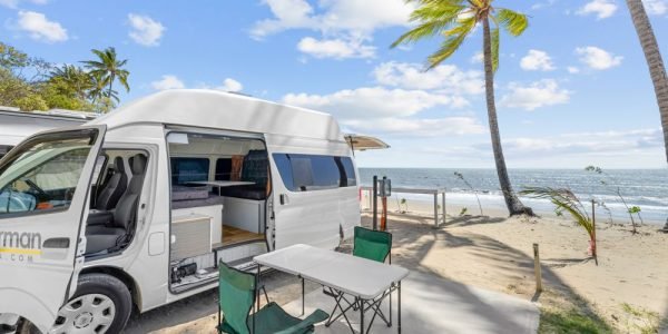 Image shows a campervan parked on the beach with all doors and windows open.