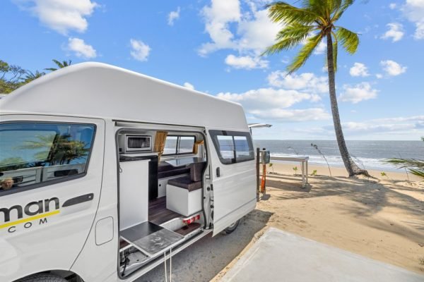 A camper van parked by a beach. The door is open to show the interior of the van.