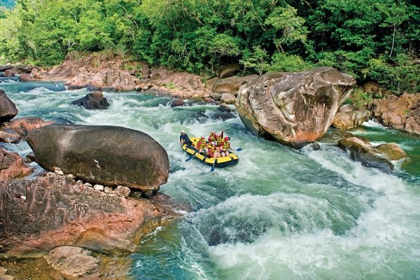 A wide shot of backpackers taking part in white water rafting in Tully, Queensland. They are approaching a rapid