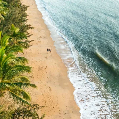 Birdseye view of beach with two people walking along.