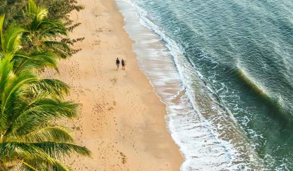 Birdseye view of beach with two people walking along.