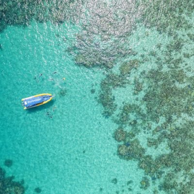 An aerial shot of a rafting boat floating in the sea surrounded by various coral formations.